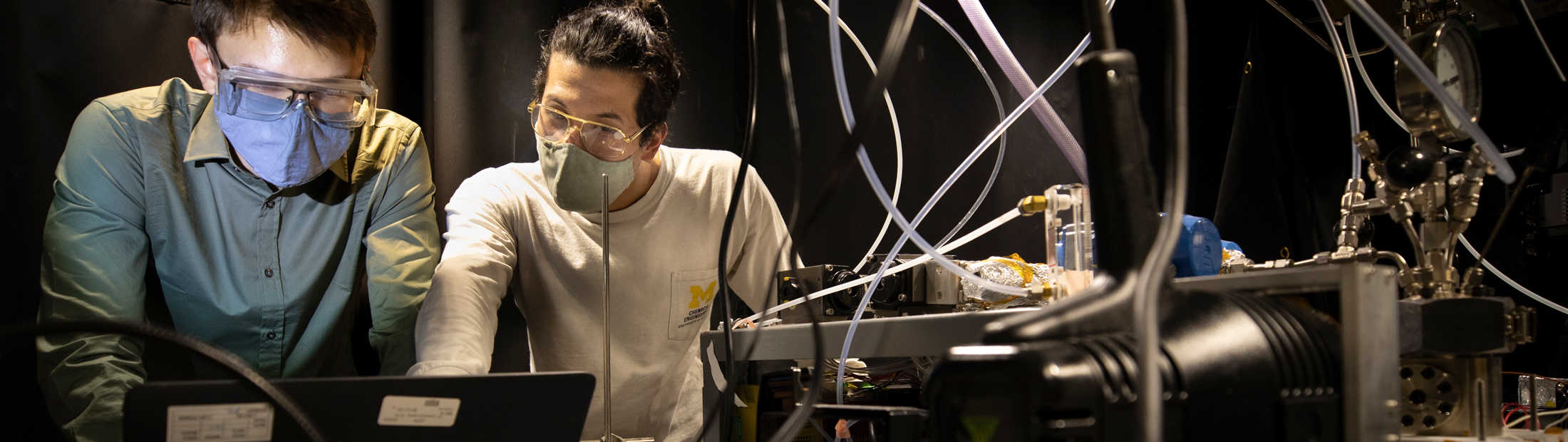 Two people standing over lab equipment and a computer, doing research